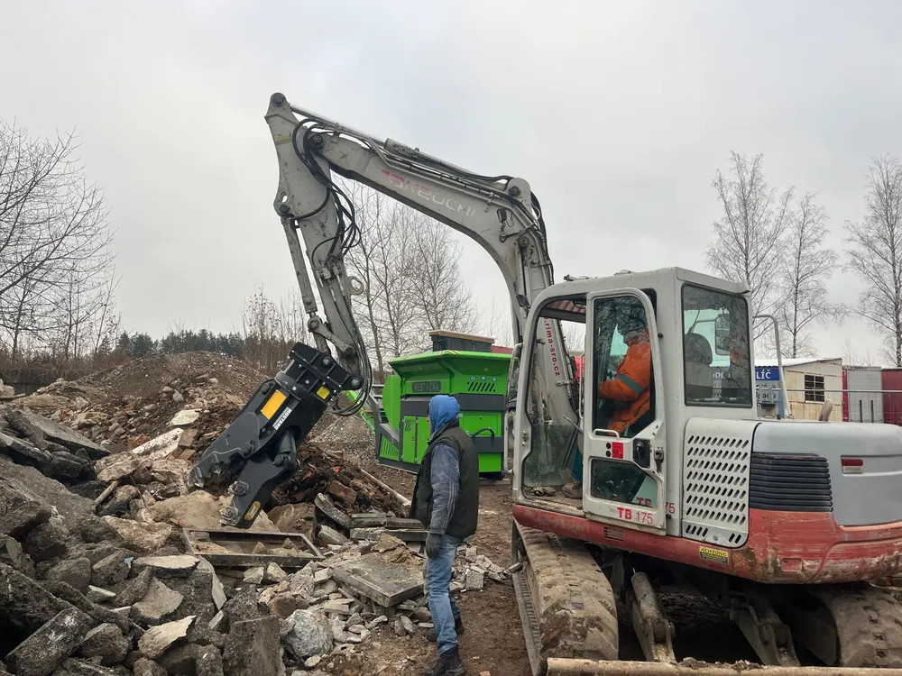 Bagr připravuje stavební suť k drcení na stavbě